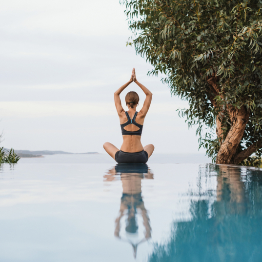 Young woman meditating. Girl is practicing yoga with sea view at background