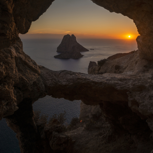 Es Vedra islet view through the rock holes of a cave at sunset, Sant Josep de Sa Talaia, Ibiza, Balearic Islands, Spain