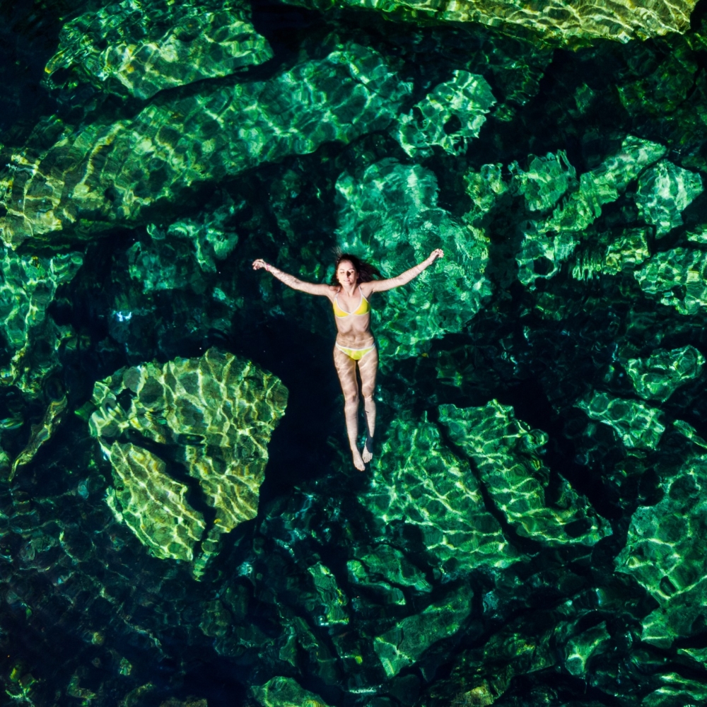 Overhead shot of a attractive young brunette woman in a bikini floating in the Cristalino cenote near Tulum, Mexico.